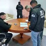 Sebastián Marset sentado en una mesa con agentes de seguridad que revisan documentos durante el operativo.