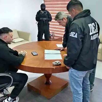 Sebastián Marset sentado en una mesa con agentes de seguridad que revisan documentos durante el operativo.