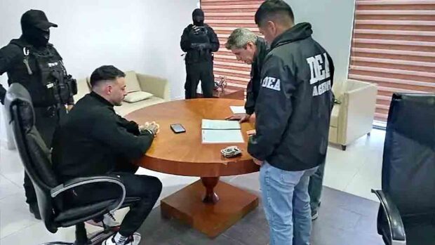 Sebastián Marset sentado en una mesa con agentes de seguridad que revisan documentos durante el operativo.